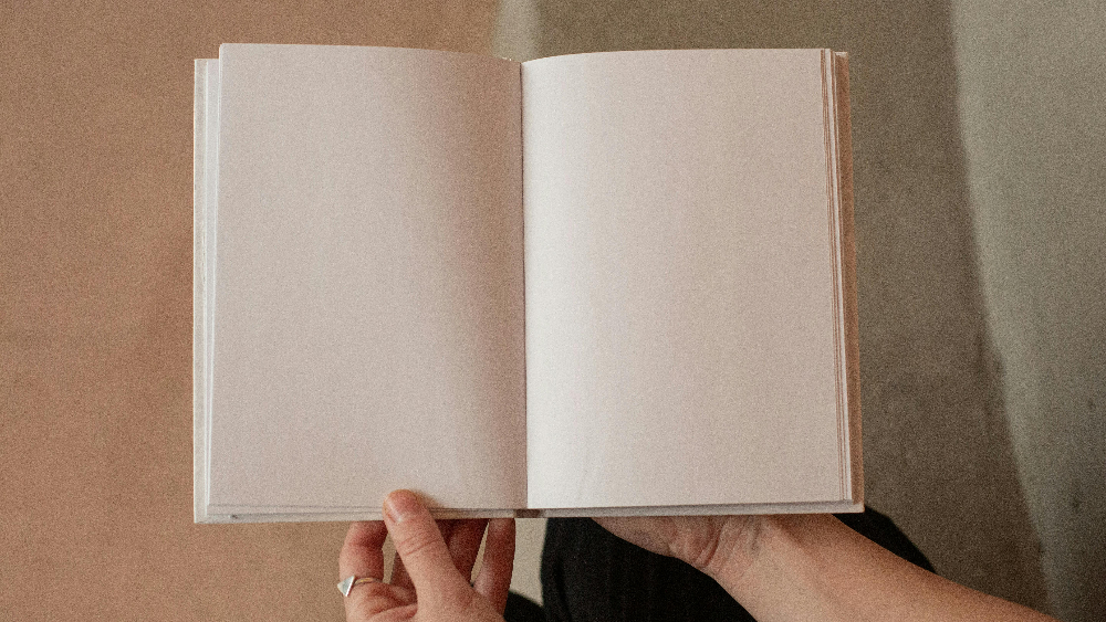 A person holding an open blank notebook with empty pages visible.